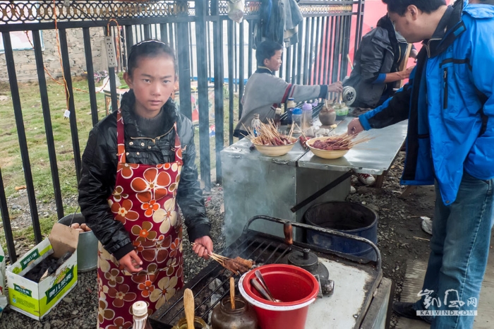 川西塔公草原木雅金顶前的广场上，一位藏族小姑娘利用双休日，帮助家人在这里卖烤肉串。