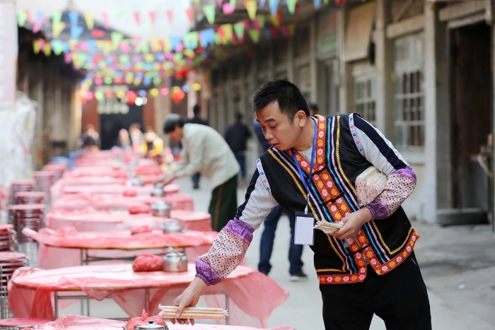 图8：2月11日，广西柳州市融安县板榄镇社区，一名社区居民在“长街宴”开始前摆放筷子。（谭凯兴 摄）