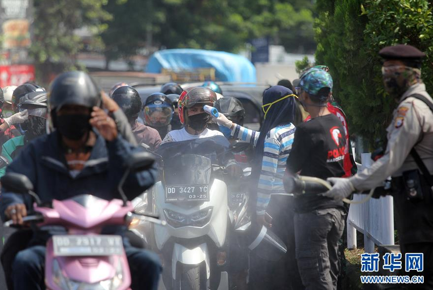 4月23日，在印度尼西亚南苏拉威西省望加锡，一名军人对来往摩托车进行消毒防疫。 新华社发（菲尔曼夏 摄）