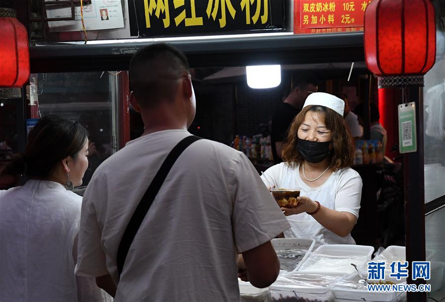 6月2日，在河南省开封市鼓楼夜市，食客从烧烤摊位前经过。 近日，河南省开封市鼓楼夜市在关闭4个月后恢复开放。近200个摊位整齐排开，各色小吃琳琅满目，烹炒的火苗、蒸腾的热气、不绝于耳的叫卖声……古色古香的广场上重现欢腾的烟火气。 新华社记者 李安 摄