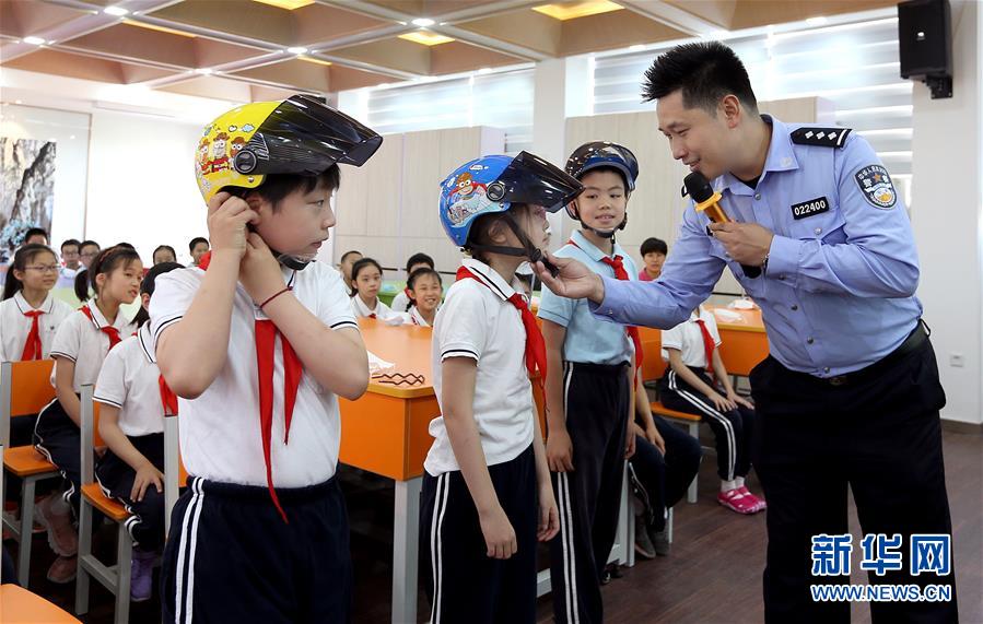 6月2日，上海市公安局徐汇分局交警支队民警韩永鑫在徐汇区逸夫小学指导小学生正确佩戴头盔。当日，上海市徐汇区40余所小学的一至三年级学生及120余所幼儿园全面复课，徐汇警方深入辖区各学校检查骑电动自行车送小学生上学的家长和学生是否佩戴头盔，提醒家长和小学生上学、放学骑行路上要正确佩戴头盔，避免意外伤害，以此提高小学生的安全意识和自我保护能力。新华社记者 凡军 摄