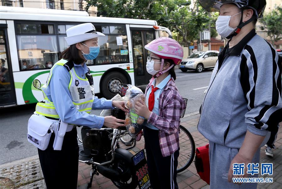 6月2日，上海市公安局徐汇分局交警支队民警朱晓菁在徐汇区逸夫小学门前，向乘坐电动自行车佩戴头盔的小学生赠送警熊玩偶。新华社记者 凡军 摄