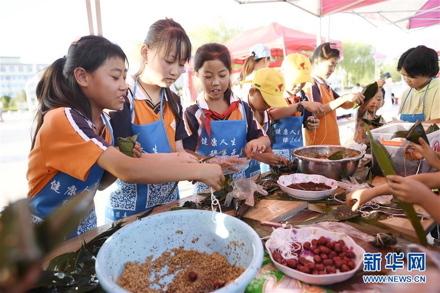 6月23日，孩子们在活动现场参加包粽子比赛。 当日，全国最大的易地生态移民扶贫集中安置区宁夏吴忠市红寺堡区举行迎端午活动，邀请各乡镇的民间剪纸、刺绣艺人现场比拼传统技艺，居民现场参与包粽子大赛，共迎端午节的到来。 新华社记者 王鹏 摄