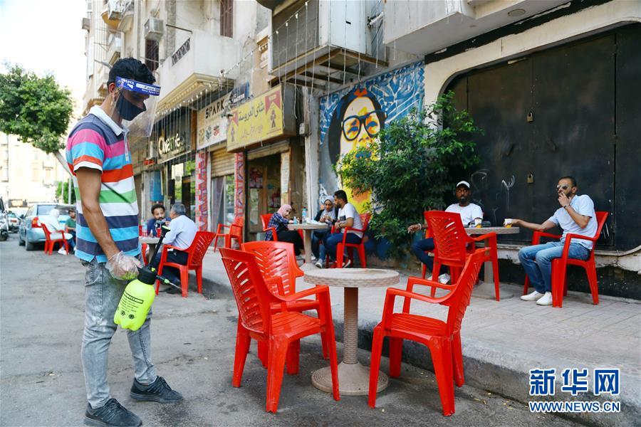 6月27日，一名男子在埃及首都开罗一家咖啡馆露天座位旁消毒。 自27日起，埃及解除部分防控措施。全国范围的宵禁时间调整为每日零时至4时，允许餐厅、咖啡馆、电影院以25%的运营能力开放并营业至22时，允许商店营业至21时。 新华社发（艾哈迈德·戈马摄）