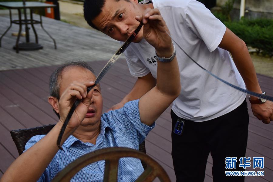 6月30日，朱生荣（左）和儿子朱强（右）在当晚电影开播前检查胶片位置。新华社记者 郑梦雨 摄