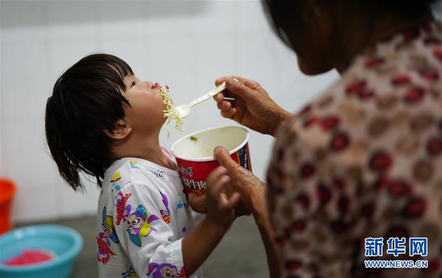 7月9日，村民在给小朋友喂饭。 当日，江西鄱阳县鄱阳镇因洪水受灾的村民被转移到多个集中安置点。在鄱阳县五一中心学校安置点，志愿者和工作人员接到任务后不到十小时内，为被转移村民布置了28间教室，供519人安顿，并为村民发放褥子、床单、枕头、盒饭、饮用水等物资。 新华社记者 周密 摄