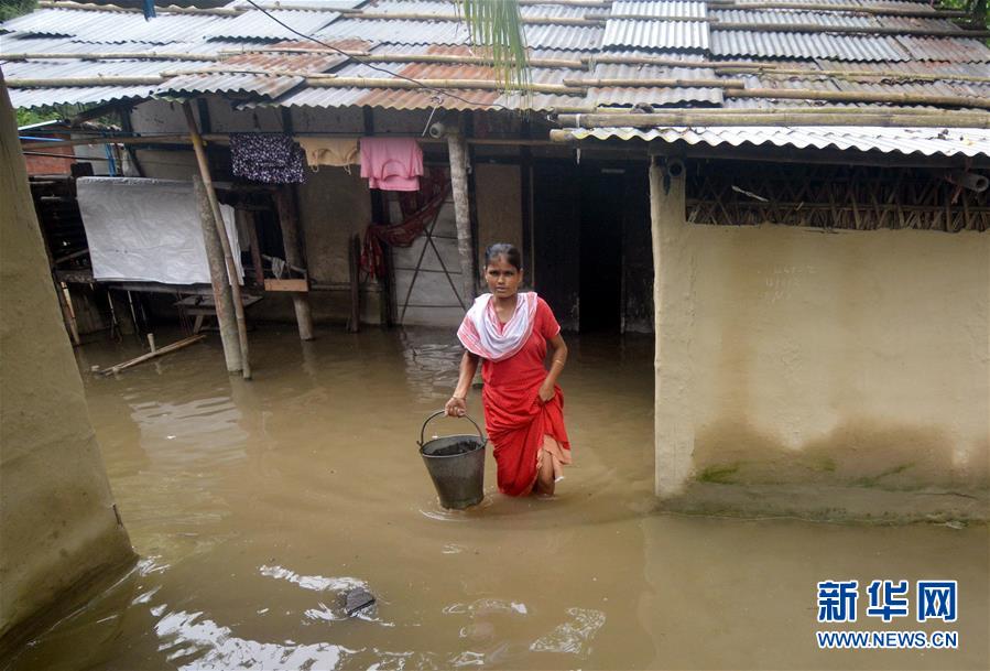 7月13日，在印度阿萨姆邦卡姆鲁普，一名女子涉水前行。 近日，印度东北部阿萨姆邦遭遇暴雨引发的洪涝灾害。 新华社发