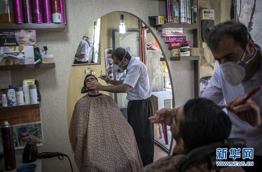 7月22日，一名男子戴着口罩在伊朗马里万的理发店为顾客服务。 伊朗卫生部22日宣布，当日新增新冠确诊病例2586例，累计确诊281413例，累计死亡14853例。 新华社发（艾哈迈德·哈拉比萨斯摄）