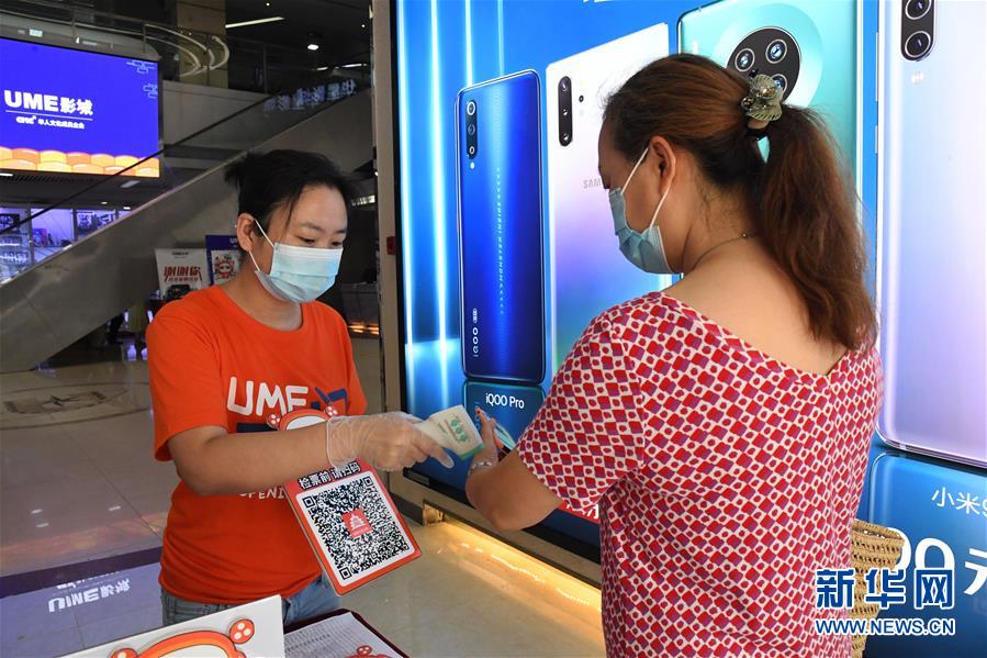7月24日，在UME影城北京华星店，工作人员（左）为观众测量体温。 当日，在做好新冠肺炎疫情防控的前提下，北京市部分电影院有序恢复开放。 新华社记者 任超 摄