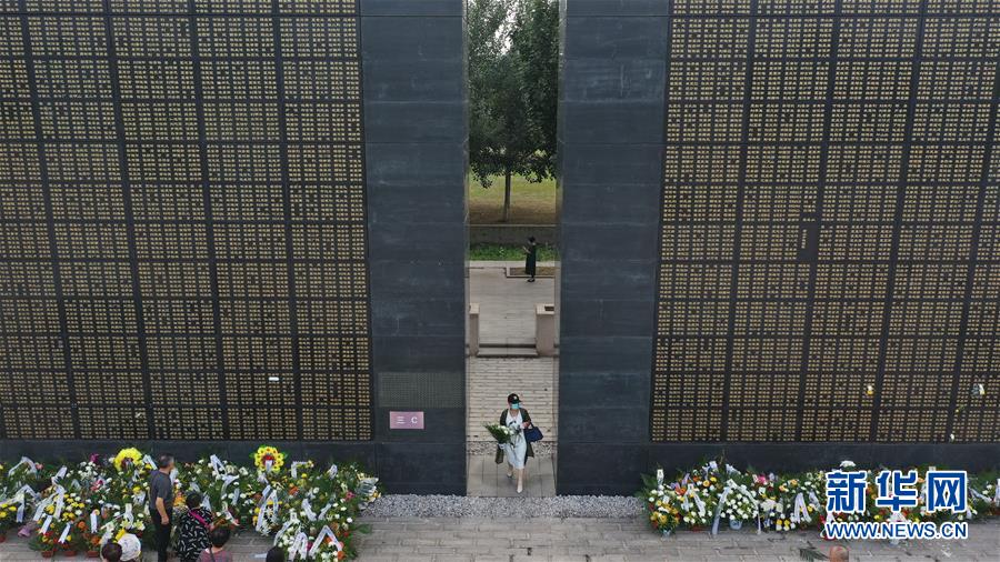 7月28日，市民拿着花从纪念墙间走过（无人机照片）。 当日是唐山大地震44周年，许多市民来到唐山地震遗址纪念公园，在纪念墙前献上鲜花，祭奠遇难的亲人。 新华社发（董军 摄）