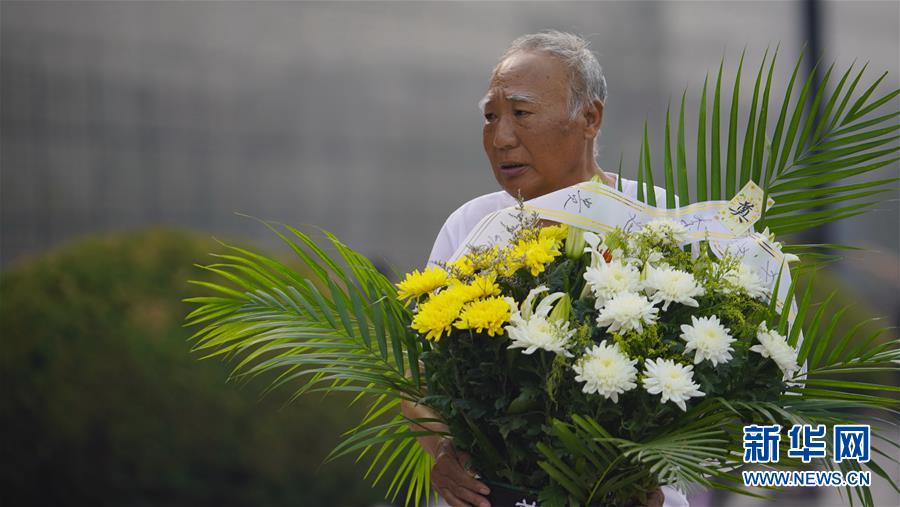 7月28日，一位市民抱着花篮从纪念墙前走过。 新华社发（董军 摄）