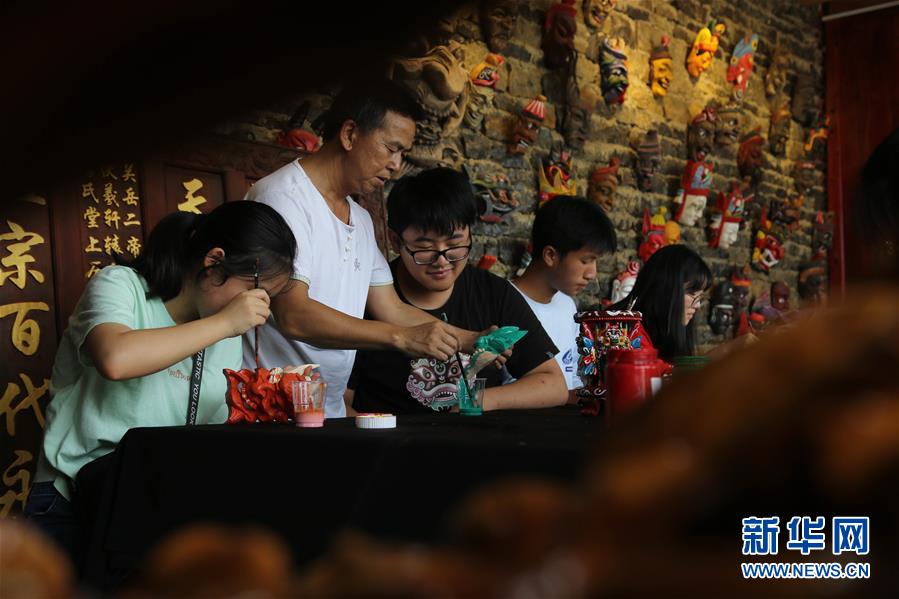 8月9日，在贵州省安顺市傩雕文化博物馆，非遗传承人秦发忠（左二）指导安顺市第一高级中学的学生给傩戏面具上色。新华社发（程洪凯 摄）