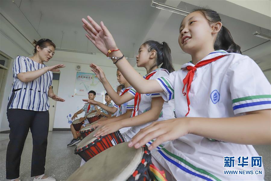 8月14日，一名老师在河北唐山遵化市东旧寨镇梁屯中心小学的活动中心指导孩子们学习打手鼓。 暑假期间，各地的孩子们通过丰富多彩的活动乐享假期、充实生活。 新华社发（刘满仓 摄）