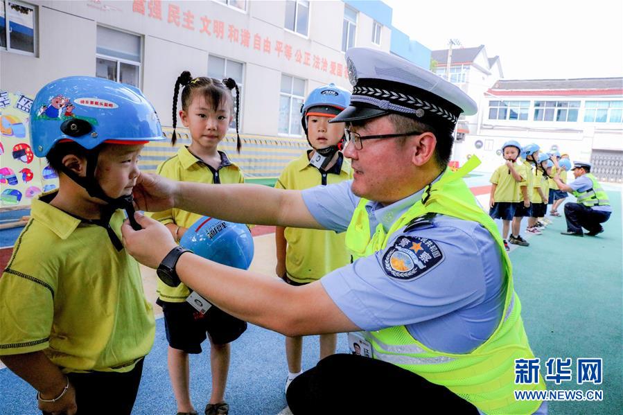 9月1日，交警给孩子们讲解如何使用安全头盔。 当日，浙江省湖州市长兴县画溪街道长桥中心幼儿园开展了以“安全‘童’行，从头做起”为主题的开学第一课活动。孩子们在交警的带领下学习交通安全知识，还进行了交通安全趣味游戏，提高交通安全意识。 新华社记者 徐昱 摄