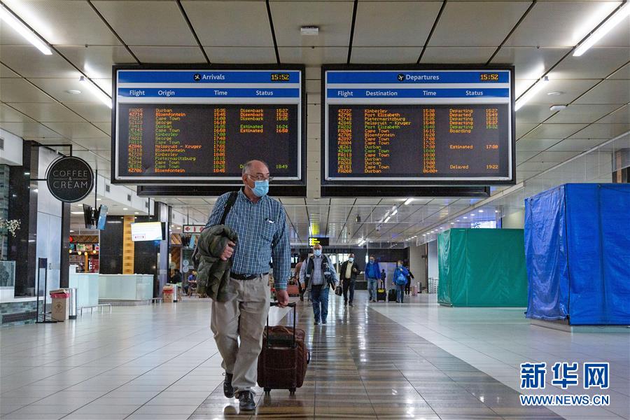 10月1日，在南非约翰内斯堡坦博国际机场，一名戴口罩的旅客从航班信息电子显示牌前走过。 新华社发（耶希尔摄）