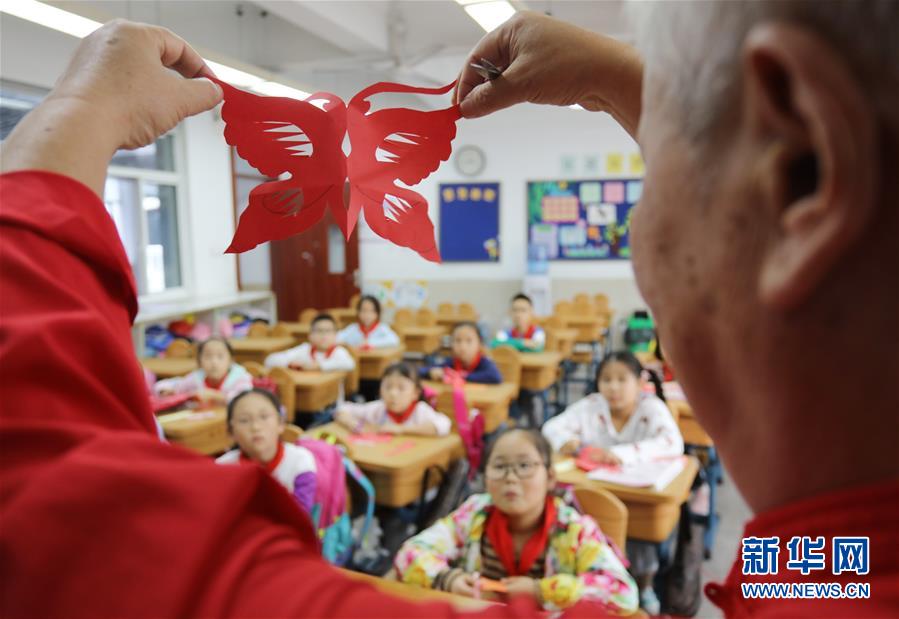 10月9日，民间艺人在苏州工业园区星海小学向孩子们讲解剪纸技艺。 当日，江苏苏州工业园区星海小学开展“传统文化手工制作体验“活动，孩子们在当地手工艺人的指导下，学习剪纸、棕编等手工技艺，感受传统文化。 新华社发（杭兴微 摄）