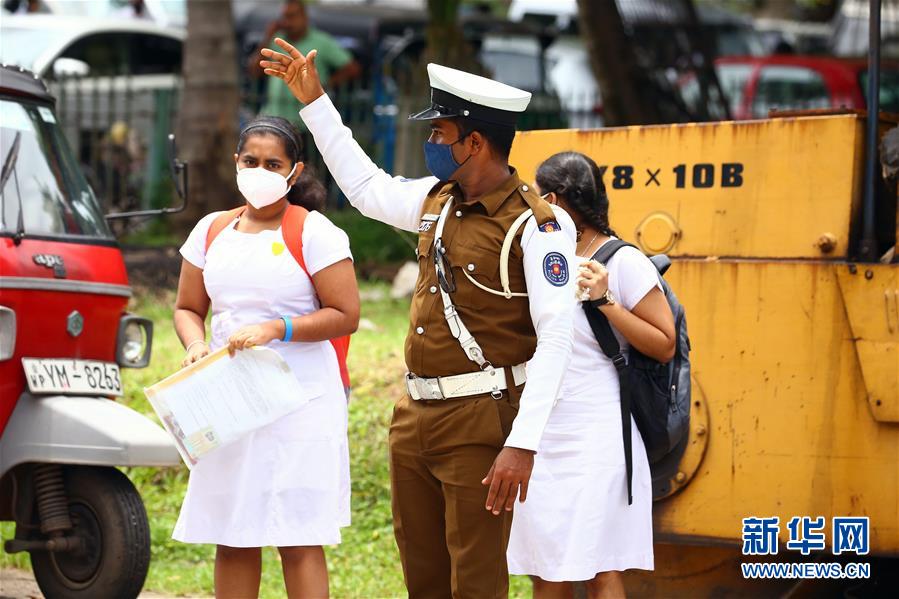 10月12日，在斯里兰卡科伦坡，警察帮助两名参加考试的女孩过马路。 当天，斯里兰卡高级程度考试在严格的防疫措施下开始举行。 新华社发（阿吉特·佩雷拉摄）