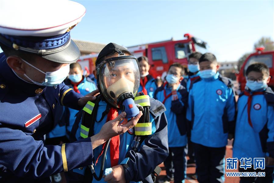 11月3日，在承德市双桥区普宁小学，学生在消防救援人员指导下体验使用正压式空气呼吸器。 当日，河北省承德市双桥区消防救援大队与普宁小学联合开展消防进校园安全互动体验教育活动。学生们通过体验救生设备、安全使用消防器材等，在互动活动中学习消防知识，提升自救能力，迎接“119消防宣传日”。 新华社发（刘环宇 摄）