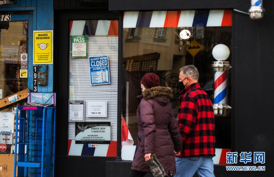 11月23日，在加拿大多伦多，戴口罩的行人路过一家关闭的理发店。当日，加拿大新增新冠确诊病例5119例，多伦多等地因疫情上升再度“封城”。新华社发（邹峥摄）