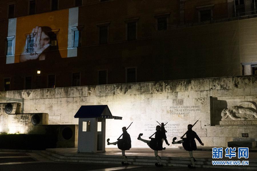 11月25日，在希腊雅典，士兵走过外墙上打出写有“反对暴力”字样投影图案的议会大厦。当日，希腊雅典在议会大厦外墙上打出写有“反对暴力”字样的投影图案，纪念国际消除对妇女暴力日。新华社发（马里奥斯·罗洛斯摄）