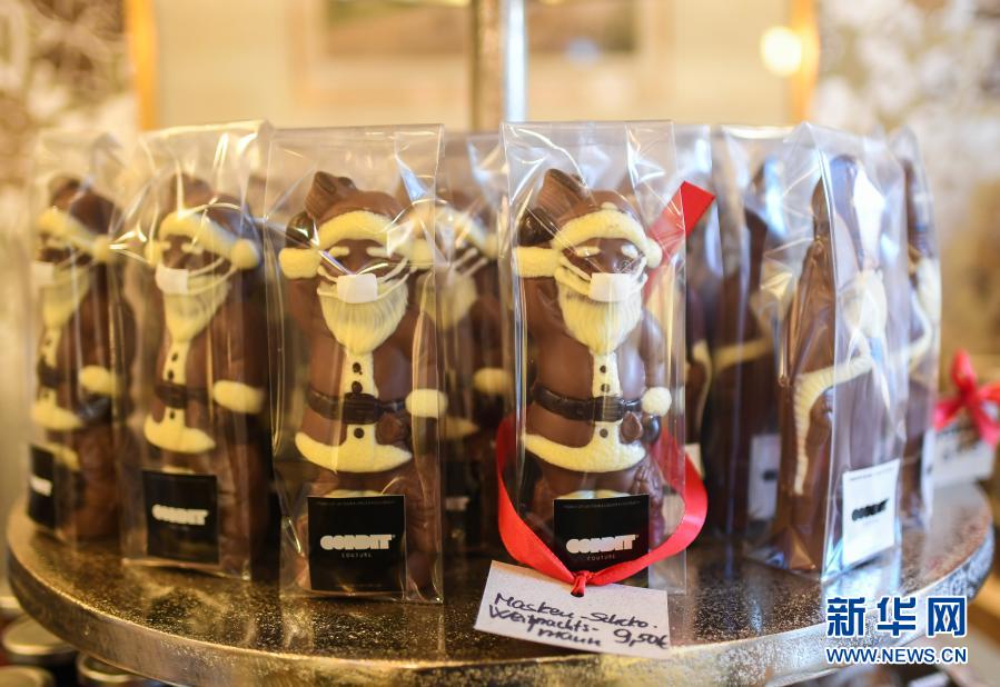 这是11月25日在德国法兰克福一家糕点店内拍摄的戴口罩的圣诞老人造型巧克力。随着圣诞节临近，德国法兰克福在当地一些街头装饰品和圣诞食品的造型设计中加入了抗疫元素，时刻提醒人们安全防疫。新华社记者逯阳摄