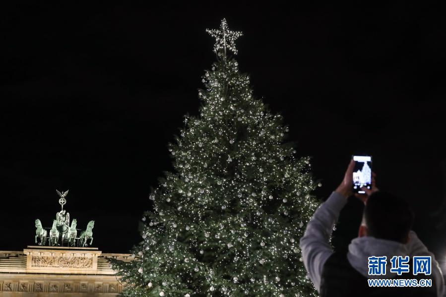 11月29日，在德国首都柏林的勃兰登堡门，一名男子拍摄被点亮的圣诞树。当日，德国柏林勃兰登堡门前的圣诞树被灯饰点亮。今年柏林多处圣诞市场及相关庆祝活动由于新冠疫情被取消。新华社记者 单宇琦 摄