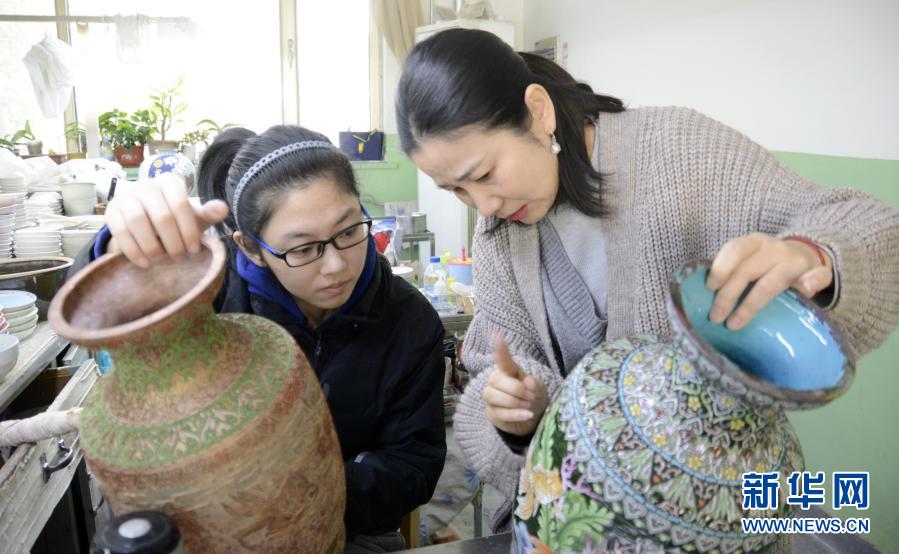 12月2日，景泰蓝技艺国家二级点蓝技师聋哑人赵楠（右）在用手语指导她的徒弟刘鸣燕昊。从2005年起，北京珐琅厂有限责任公司开始招收聋哑人技工，经过老技师们的精心培养，目前有17位聋哑人成为景泰蓝技师，有些还成为景泰蓝技艺国家二级技师。通过学习景泰蓝技艺，这些聋哑人在无声的世界里有了一个多彩的人生。新华社记者 李欣 摄