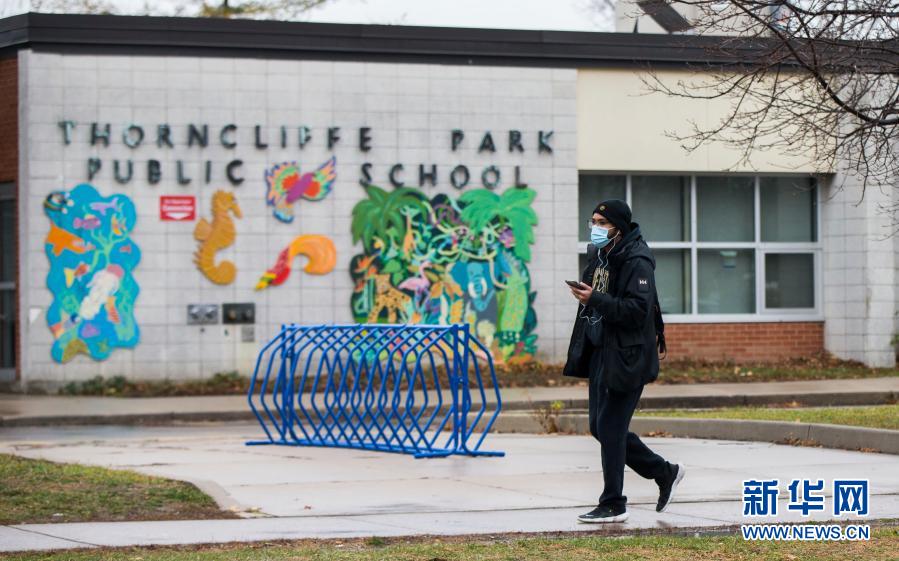 12月4日，在加拿大多伦多，一名戴口罩的男子从一所因新冠疫情暂时关闭的学校前走过。截至当日下午，加拿大累计新冠确诊病例升至400031例，累计死亡12470例。新华社发（邹峥摄）