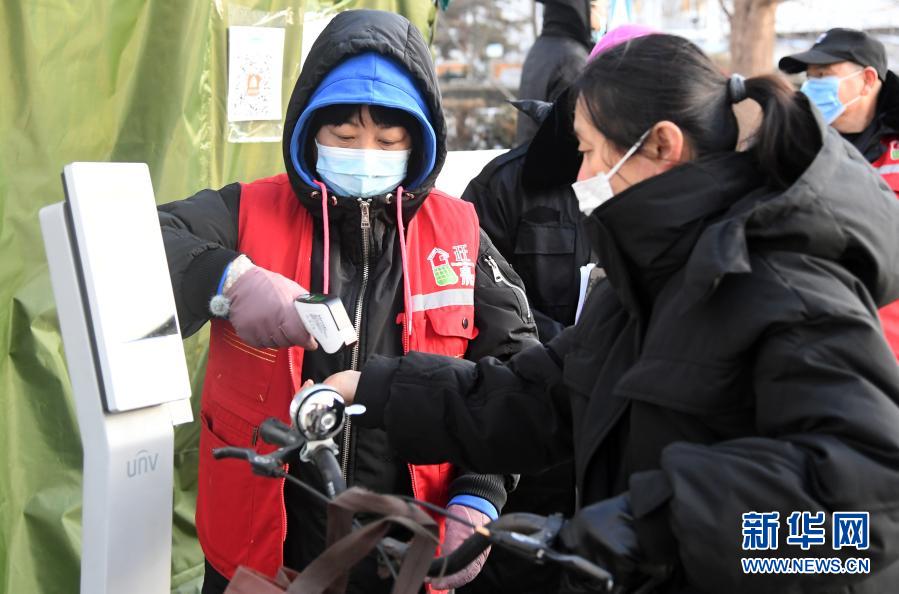 12月29日，在北京市顺义区旺泉街道宏城花园社区出入口，社区工作人员（左）为居民测量体温。近日，北京市顺义区旺泉街道宏城花园社区加强疫情防控力度，对进入社区人员和车辆进行排查，对进入社区人员进行测温、检查北京健康宝等，严防社区传播风险。新华社记者 任超 摄