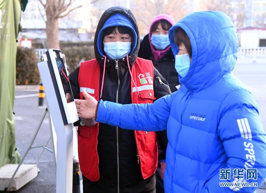 12月29日，在北京市顺义区旺泉街道宏城花园社区出入口，社区工作人员（左）指导居民测量体温。新华社记者 任超 摄