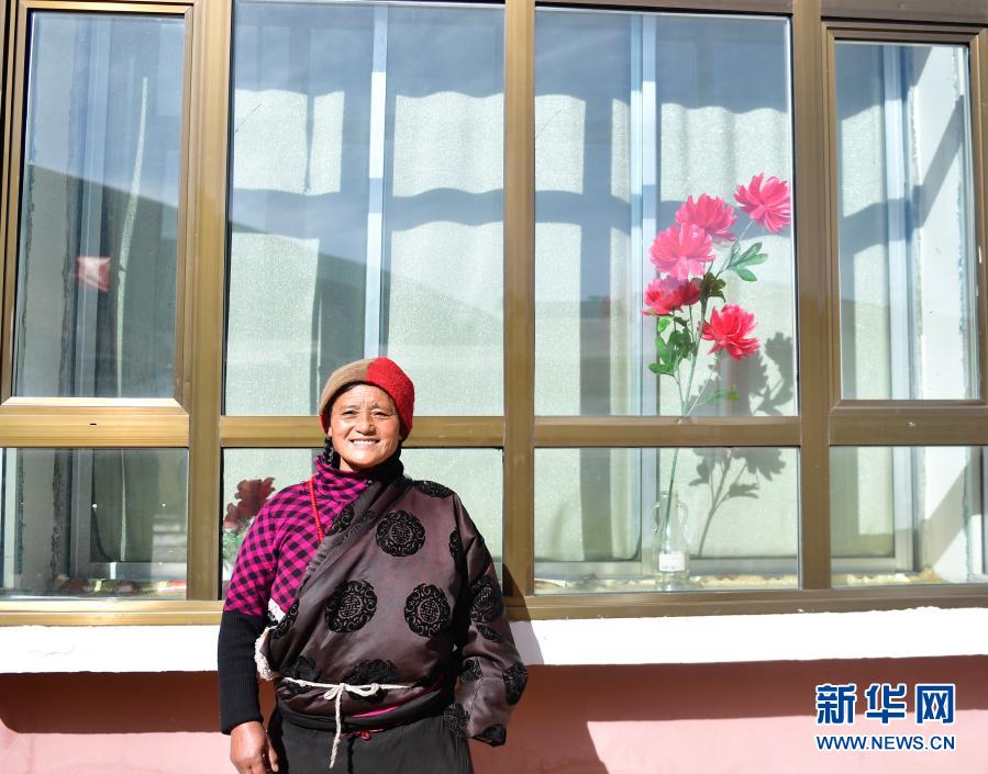 1月11日，隆亚村牧民索吉在搬迁点的新家前留影。青海省果洛藏族自治州甘德县上贡麻乡隆亚村的67户牧民曾经是建档立卡贫困户，他们分散居住在大山深处，交通不便，生活条件恶劣。2016年，当地对隆亚村实施易地搬迁，集中安置。新建的搬迁点不仅交通便利、水电俱全，而且村里安装了风力发电机组70台，搬迁户院内修建了阳光房，安装了太阳能光伏电板。牧民们一方面通过发展风光互补产业增收，一方面成为生态管护员，在保护环境的同时也有稳定收入。新华社记者 张龙 摄