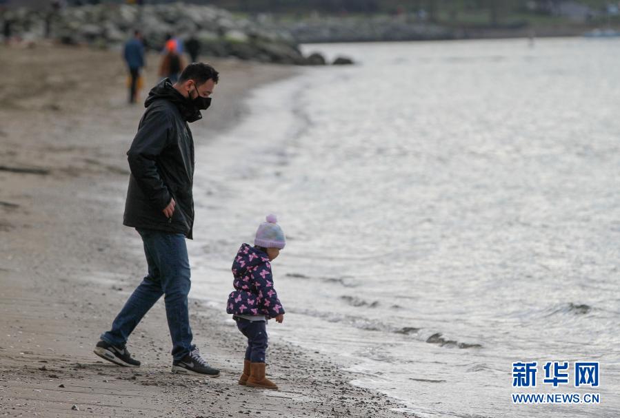 1月17日，在加拿大温哥华，一名戴口罩的男子带着孩子在海边散步。截至当地时间16日中午，加拿大累计新冠确诊病例已超过70万例。在疫情下，温哥华仍有不少民众到海滩和公园散步，舒缓应对疫情的生活压力。新华社发（梁森摄）