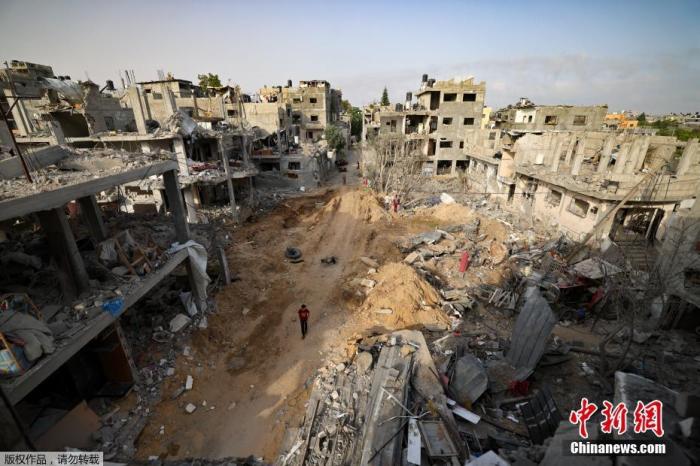 当地时间5月21日,加沙地带,一名男子在被炸毁的废墟中行走。 点击进入下一页