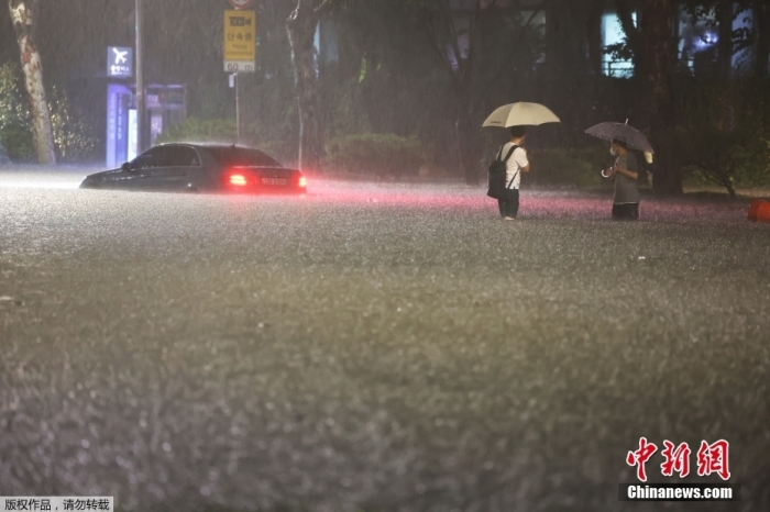 当地时间2022年8月8日，韩国首尔遭遇特大暴雨。截至8日21时，首尔部分地区降雨量在1个小时内达到141.5毫米，超过了有相关记录以来首尔每小时降雨量的历史最高值。首尔多个地段被水淹没，多条地铁线路区间运行或停运，还接连发生地面沉降、停电等事故。韩国行政安全部当天21时30分将灾害危机警报从“注意级”上调至“警戒级”。图为首尔江南区，行人和车辆涉水出行。